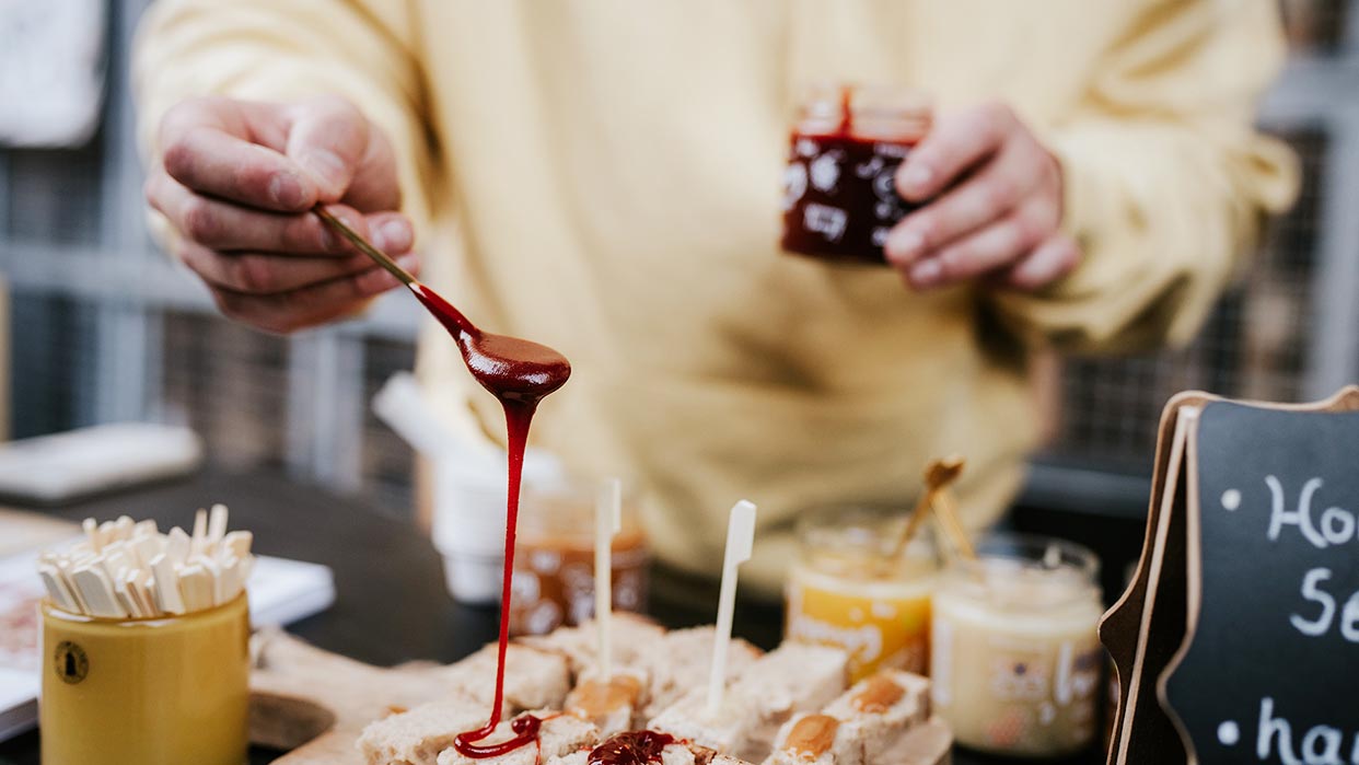 Person gießt Fruchtsauce über kleine Gebäckwürfel auf einem Verkostungstisch bei eat & Style Hamburg.