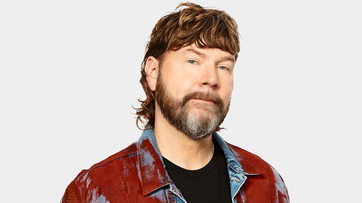 Rea Garvey mit schulterlangem, gewelltem Haar trägt eine rote Jacke mit blauen Jeansstoffdetails über einem schwarzen T-Shirt.