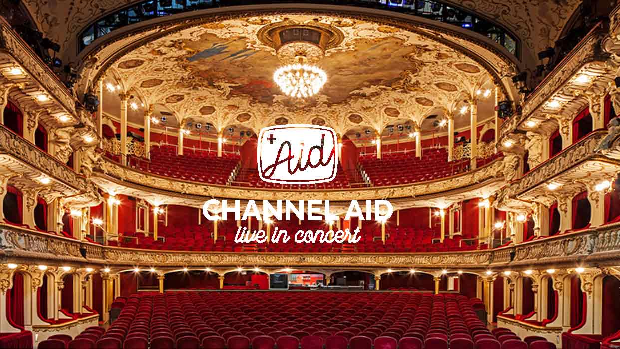 Prunkvoller Konzertsaal mit rotem Sitzbereich, goldverzierten Balkonen und einem großen Kronleuchter an der bemalten Decke, darüber das Logo 'Aid' und der Text 'CHANNEL AID live in concert'.