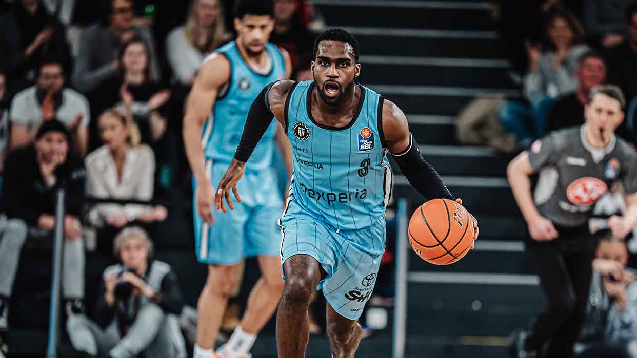 Basketballspieler der Veolia Towers Hamburg dribbelt den Ball während eines Spiels in hellblauem Trikot mit der Nummer 3.