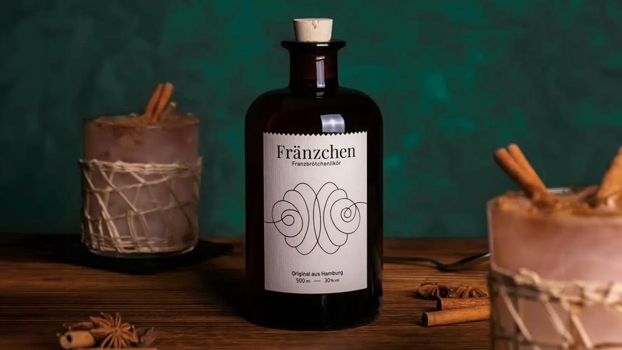 Braune Glasflasche mit Aufschrift 'Fränzchen' und zwei Kerzen mit Gewürzstangen auf einem Holztisch.