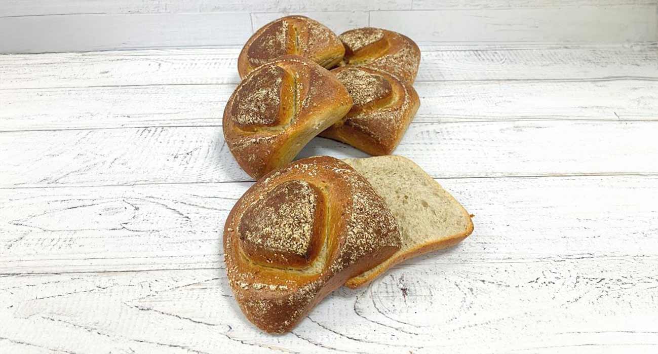 Fünf Buchweizenbrötchen, eines davon aufgeschnitten, liegen auf einer weißen Holzoberfläche.