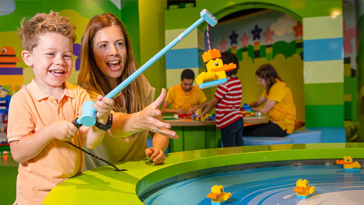 Kind und Mutter im LEGO Discovery Centre Hamburg bedienen eine Angel mit LEGO-Enten über einem Wasserbecken mit weiteren LEGO-Enten.