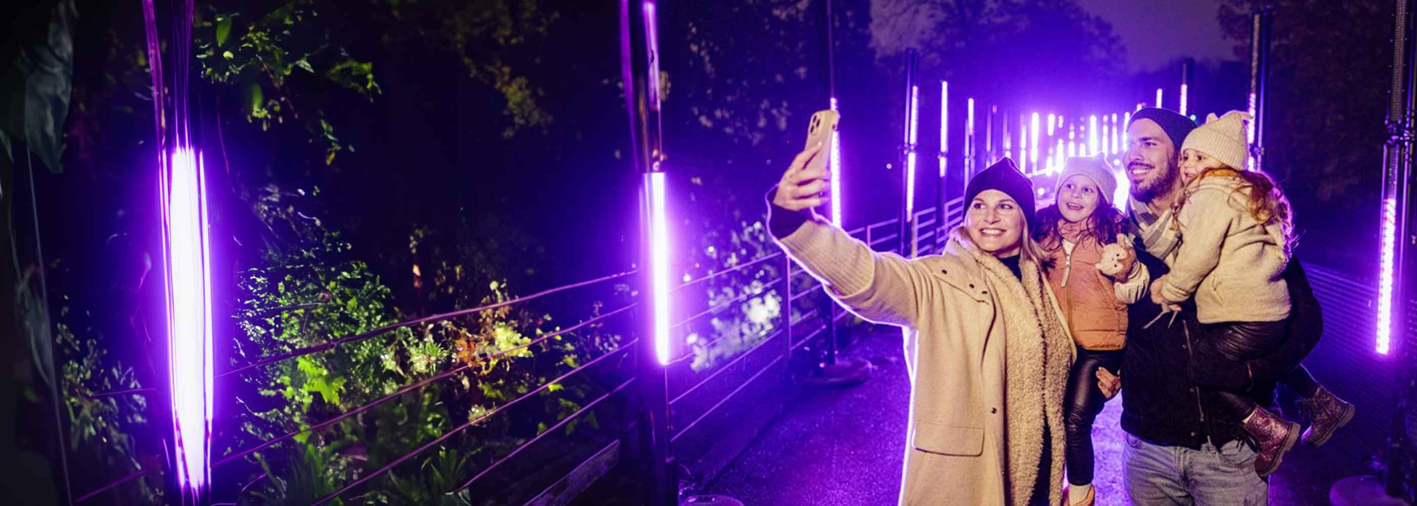 Familie mit zwei Kindern macht Selfie auf beleuchtetem Weg im Christmas Garden Hamburg bei Nacht.