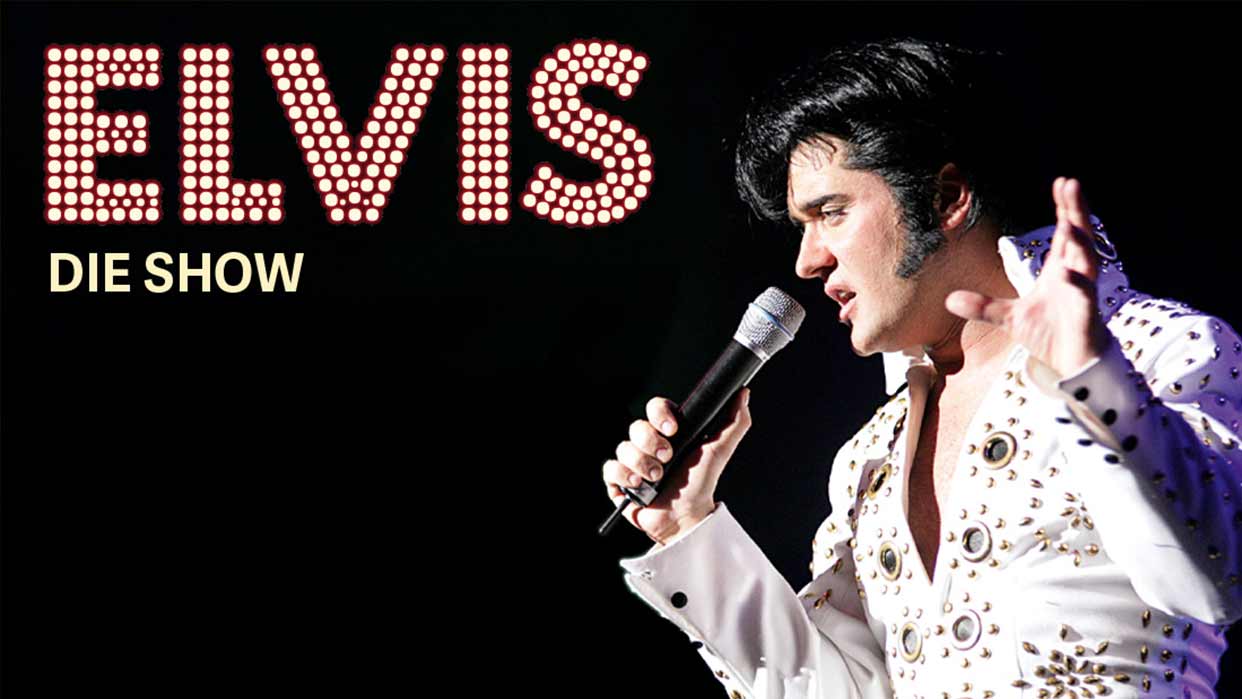 Sänger in weißem, mit Schmucksteinen besetztem Bühnenanzug hält Mikrofon und gestikuliert vor schwarzem Hintergrund mit Schriftzug 'ELVIS DIE SHOW'.