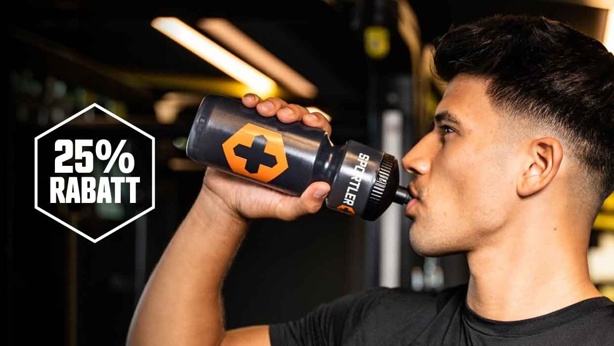 Person mit kurzem, dunklem Haar trinkt aus einer schwarzen Sportflasche mit orangefarbenem Kreuz und Aufschrift 'SSPORTLER' in einer Fitnessumgebung.