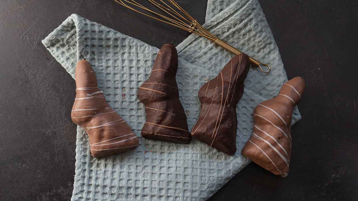 Vier schokoladenüberzogene Hasenmuffins mit weißer Zierglasur liegen auf einem hellblauen Waffeltuch neben einem Schneebesen.