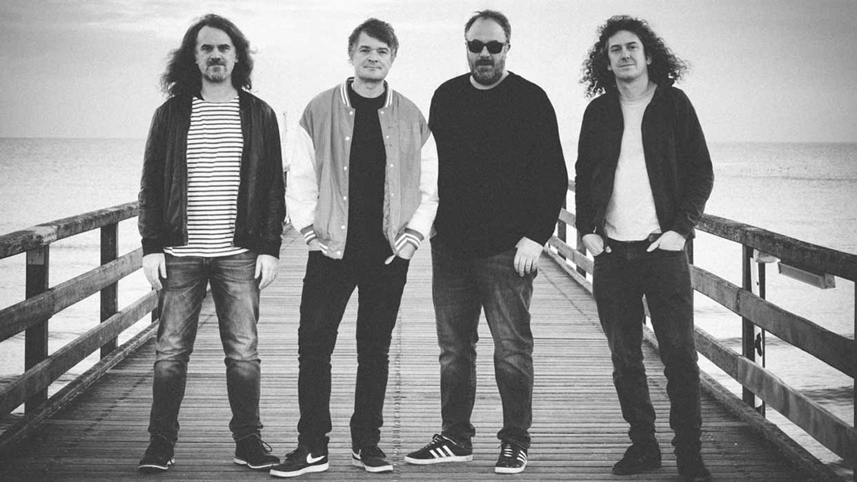 Die Band Madson (vier Männer) stehen nebeneinander auf einem Steg am Wasser, alle tragen Freizeitkleidung mit Jacken und Jeans.