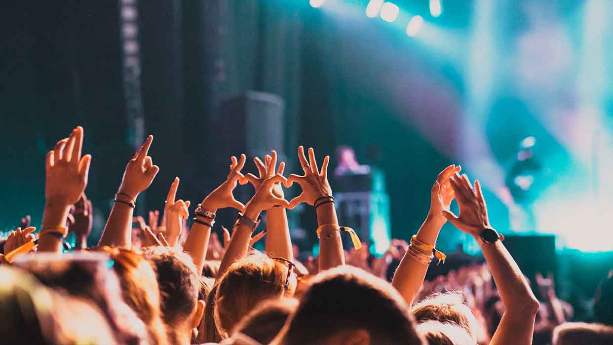 Menschenmenge bei Konzert hebt Hände und bildet Herzen mit den Fingern vor Bühne.