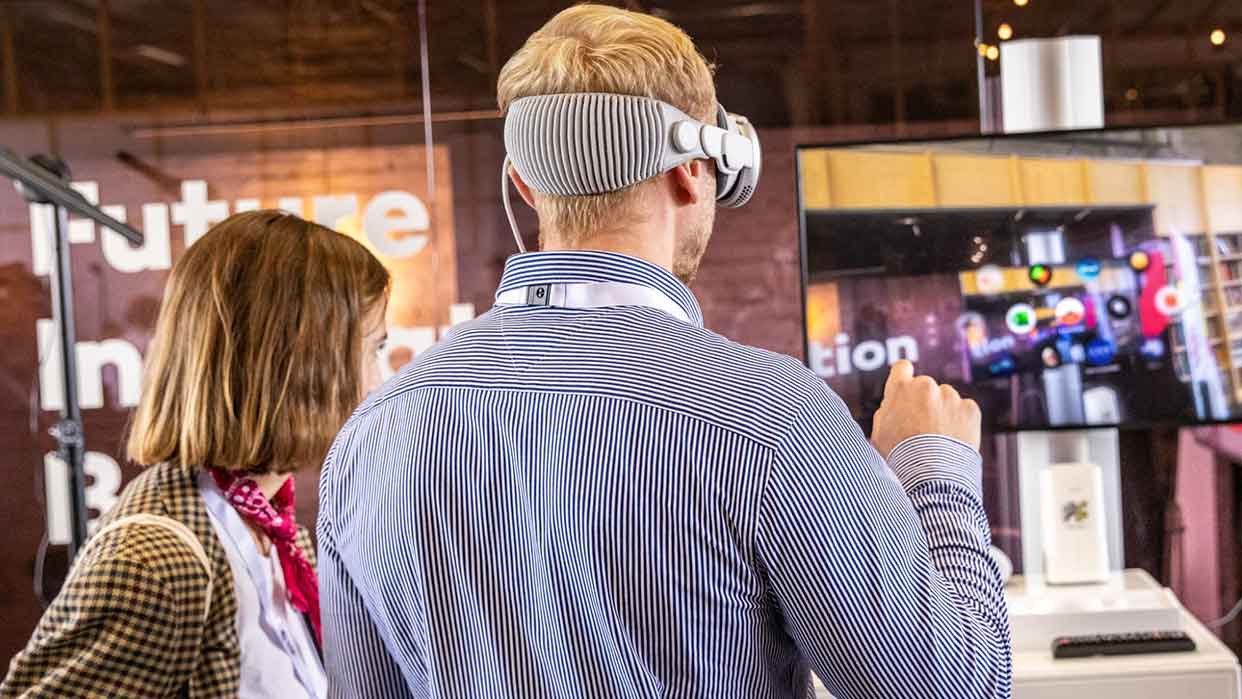 Mann mit Virtual-Reality-Brille interagiert mit digitaler Präsentation auf dem Hamburg Innovation Summit, Frau beobachtet.