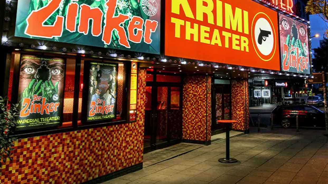 Theaterfassade mit leuchtendem Schriftzug 'Zinker' und 'KRIMI THEATER' sowie Plakaten mit grünem Gesicht und Text 'Der Zinker IMPERIAL THEATER'.