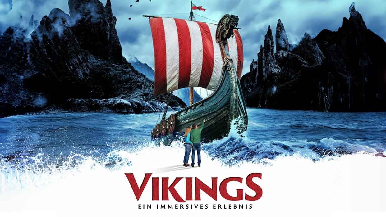 Ein Wikingerschiff mit rotem und weißen Segel fährt durch stürmisches Wasser. Im Hintergrund sind dunkle Berge und ein klarer Himmel zu sehen. Text: 'VIKINGS EIN IMMERSIVES ERLEBNIS'.