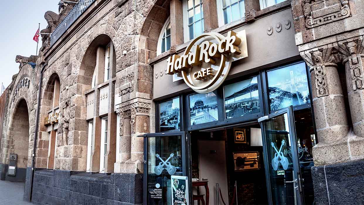 Eingang des Hard Rock Cafe Hamburg mit beleuchtetem Logo über dem Türrahmen und zwei großen Fenstern mit Gitarrenmotiven.