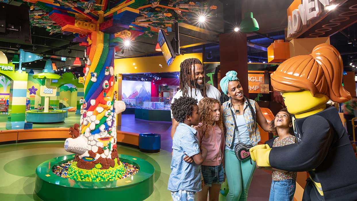 Kinder stehen im LEGO Discovery Centre Hamburg vor einer großen, bunten LEGO-Skulptur und interagieren mit einer lebensgroßen LEGO-Figur mit rotem Pferdeschwanz.