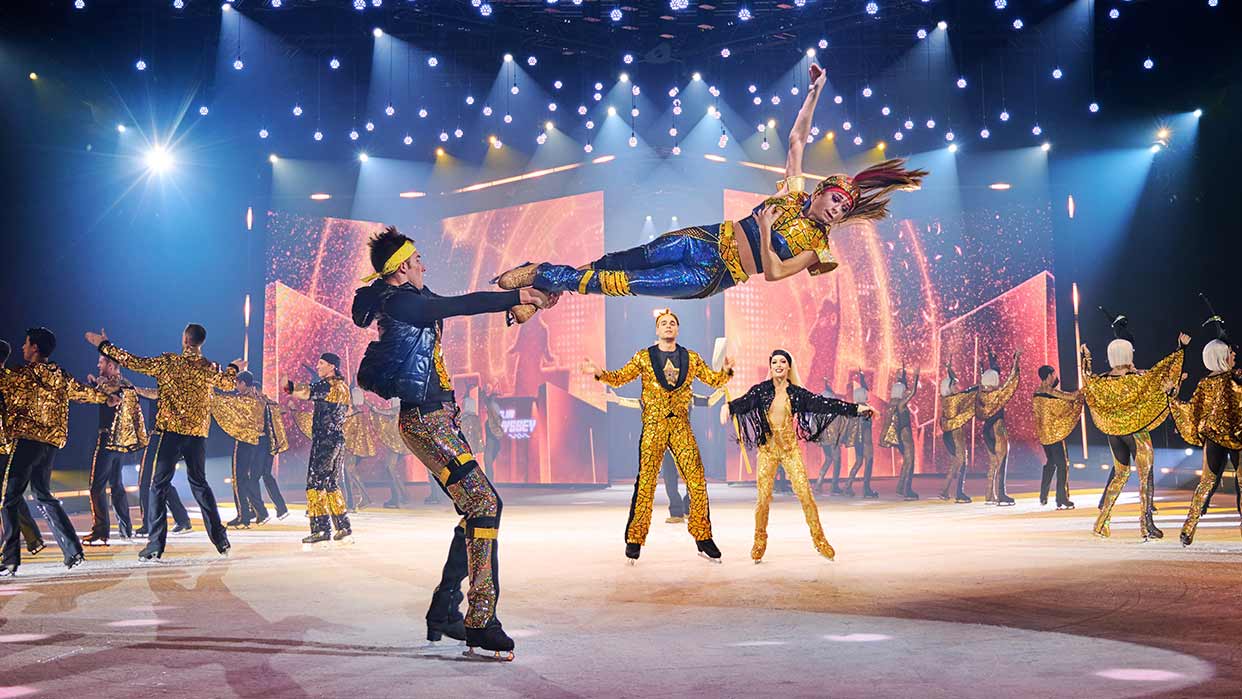 Holiday on Ice Show mit Eiskunstläufern in gold-blauen Kostümen, eine Frau wird hoch in der Luft gehalten.